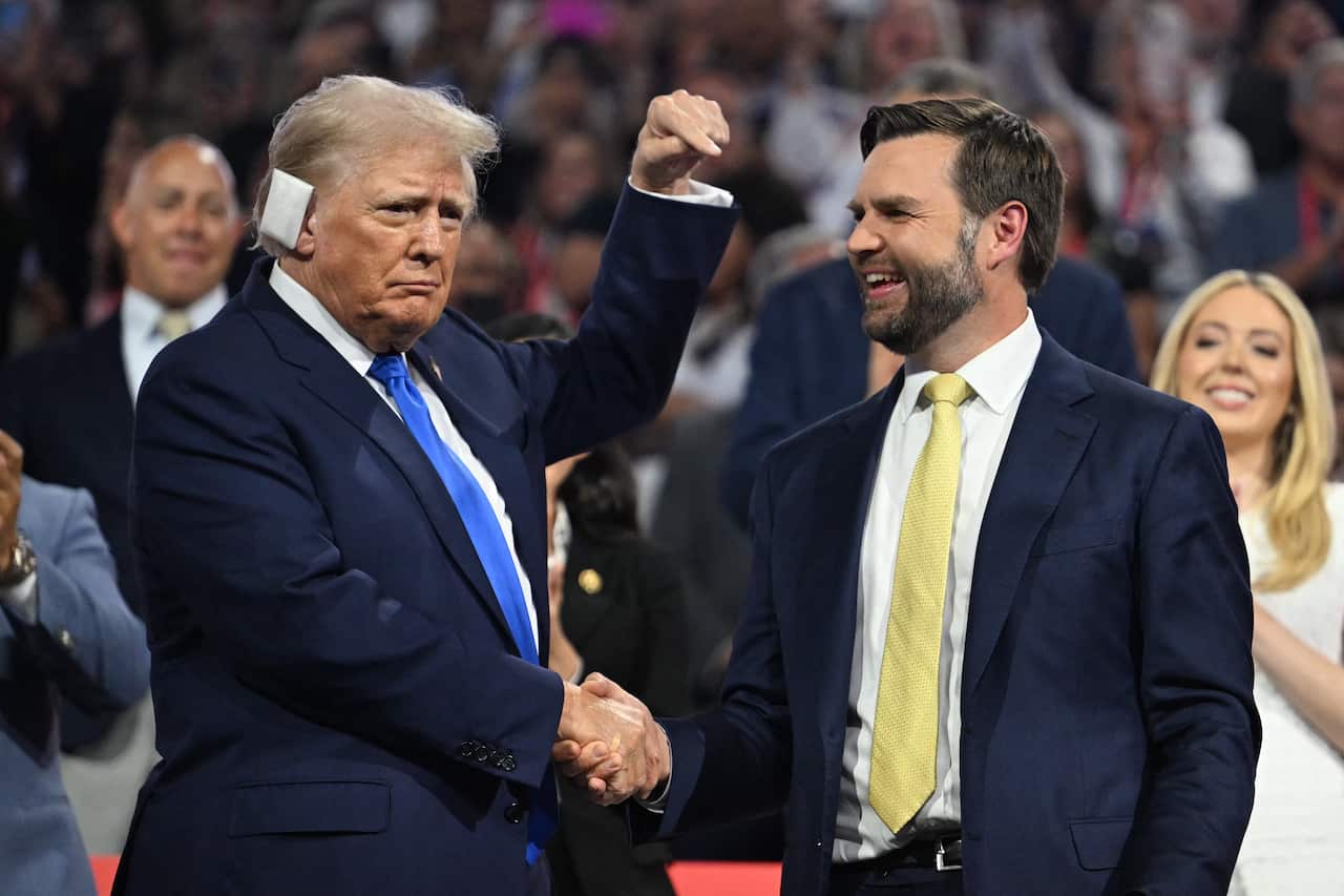 Donald Trump and JD Vance hold hands in front of a cheering crowd, with Trump pointing at Vance.