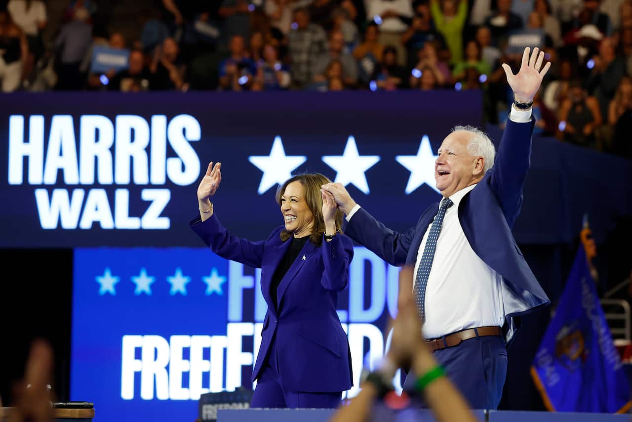Kamala Harris and Tim Walz stand on stage, holding hands and raising them in the air as they wave to the crowd and share a laugh.